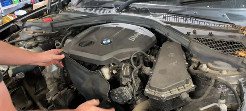 Removing the plastic engine cover from the BMW 116d to reach the auxiliary belt