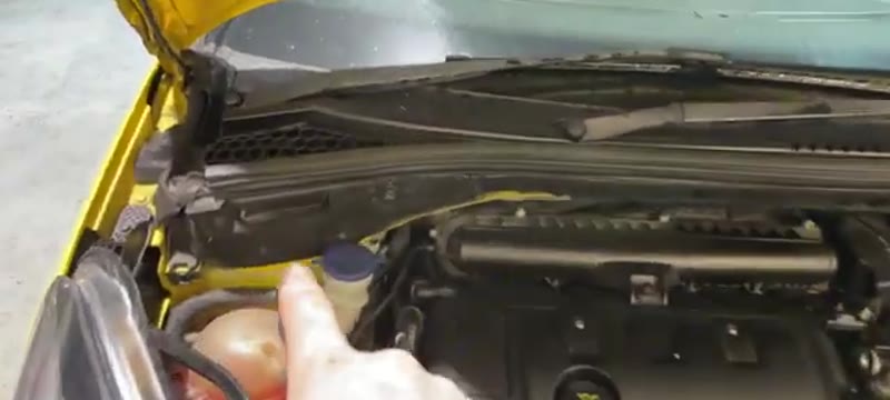Engine bay of a yellow Citroën DS3 with the bonnet open, showing where the pollen filter housing cover sits near the passenger-side firewall