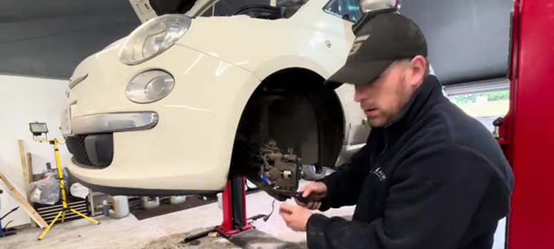 Using pliers to pull the safety clip from the bottom of the Fiat 500 brake caliper