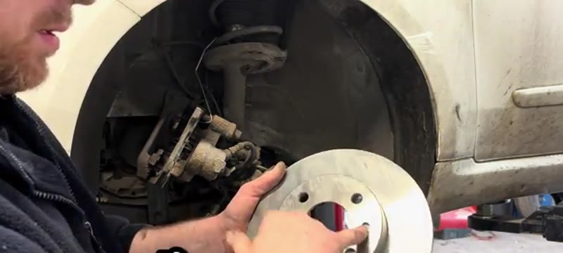Holding the new brake disc up to the Fiat 500 hub, lining up the locating holes