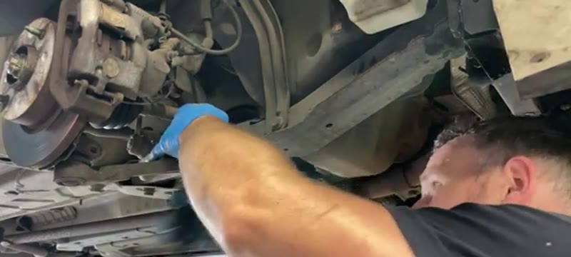 Undoing the underbody brace bar bolts from beneath the Fiat 500 on a ramp