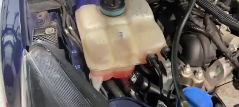 Coolant expansion tank and surrounding engine bay on a Ford Focus, checked for hairline cracks and staining