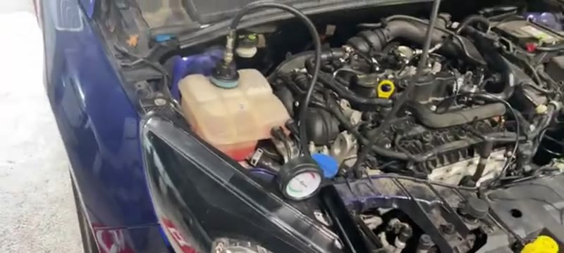 Cooling system pressure tester fitted to the expansion tank of a Ford Focus with the gauge showing system pressure