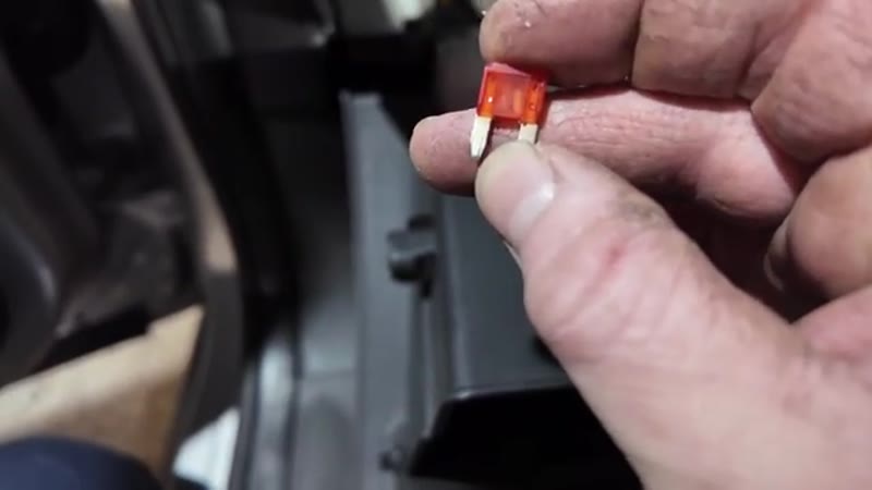 Holding the blown 10 amp fuse up to the light to inspect the broken wire inside