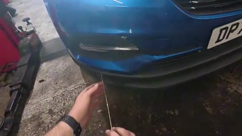 Pressing a mechanic's stethoscope probe against a parking sensor in the front bumper