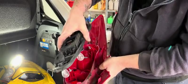 Releasing the tabs on the Vauxhall Corsa bulb holder to access the brake light bulb
