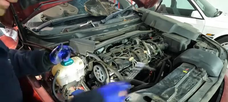Undoing the 10mm water pump bolts on the Volvo XC90 D5 with a tray ready for coolant