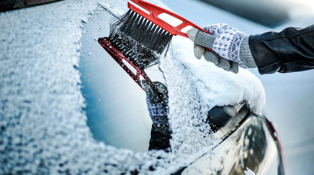 Person clearing snow from a car windscreen in winter